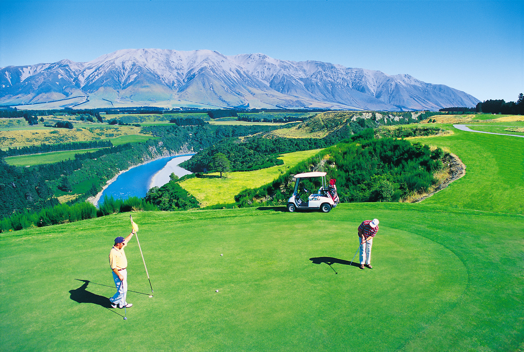Two people playing golf with scenic mountains in background.
